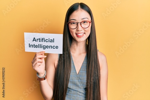 Young chinese woman holding artificial intelligence paper looking positive and happy standing and smiling with a confident smile showing teeth