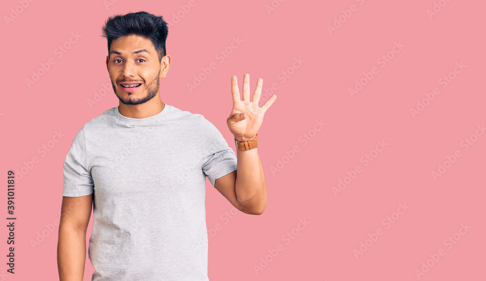 Naklejka premium Handsome latin american young man wearing casual tshirt showing and pointing up with fingers number four while smiling confident and happy.