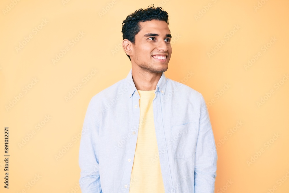 Young handsome hispanic man standing over yellow background looking to side, relax profile pose with natural face and confident smile. - obrazy, fototapety, plakaty 