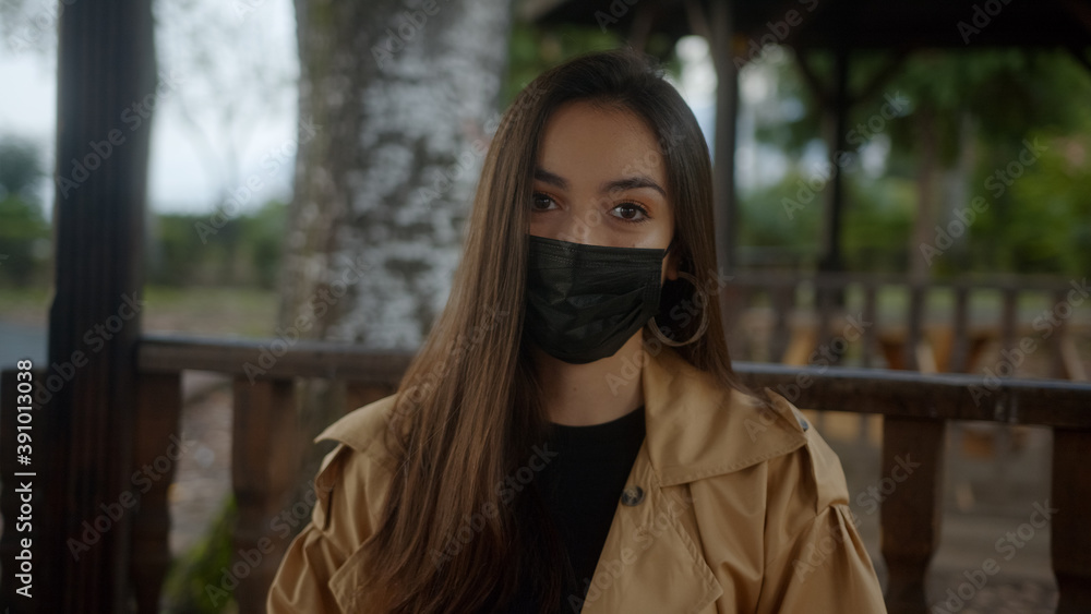 Beautiful woman wearing black mask, sitting on a bench during pandemic period and she is taking off her mask and breathing and smiling while looking at camera, lifestyle and pandemic covid-19 Beautiful woman wearing black mask, sitting on a bench during pandemic period and she is taking off her mask and breathing and smiling while looking at camera, lifestyle and pandemic covid-19