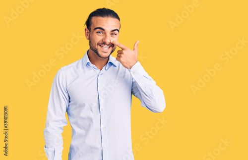 Young handsome man wearing business clothes pointing with hand finger to face and nose, smiling cheerful. beauty concept