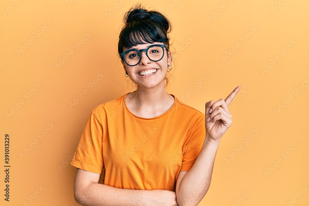 Young hispanic girl wearing casual clothes and glasses smiling happy pointing with hand and finger to the side Young hispanic girl wearing casual clothes and glasses smiling happy pointing with hand and finger to the side