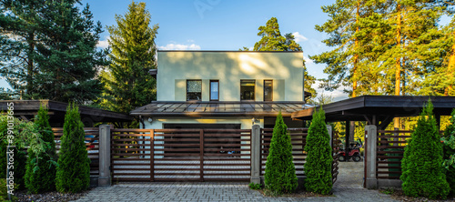 Exterior of luxury private house at sunny summer day. Green pines. Thujas at modern fence.