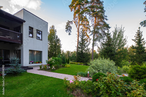 Fototapeta Naklejka Na Ścianę i Meble -  Modern exterior of private cottage near the pine forest. View of beautiful garden with flowers, bushes and trees.