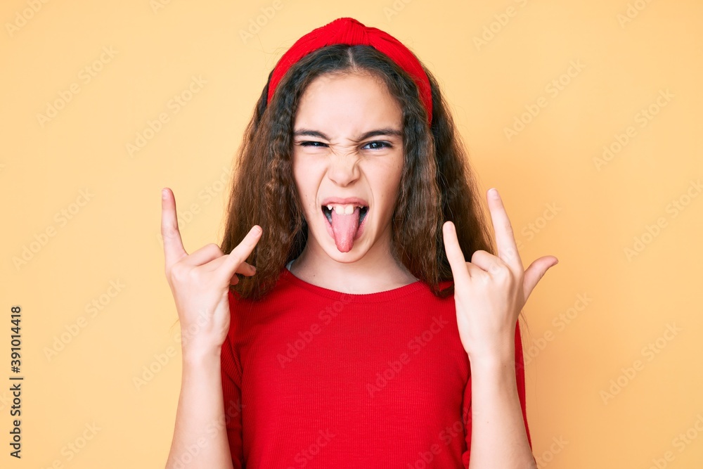 Cute hispanic child girl wearing casual clothes and diadem shouting with crazy expression doing rock symbol with hands up. music star. heavy concept. Cute hispanic child girl wearing casual clothes and diadem shouting with crazy expression doing rock symbol with hands up. music star. heavy concept.