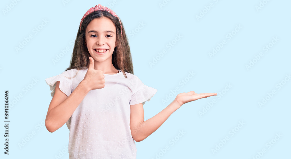 Cute hispanic child girl wearing casual white tshirt showing palm hand and doing ok gesture with thumbs up, smiling happy and cheerful Cute hispanic child girl wearing casual white tshirt showing palm hand and doing ok gesture with thumbs up, smiling happy and cheerful