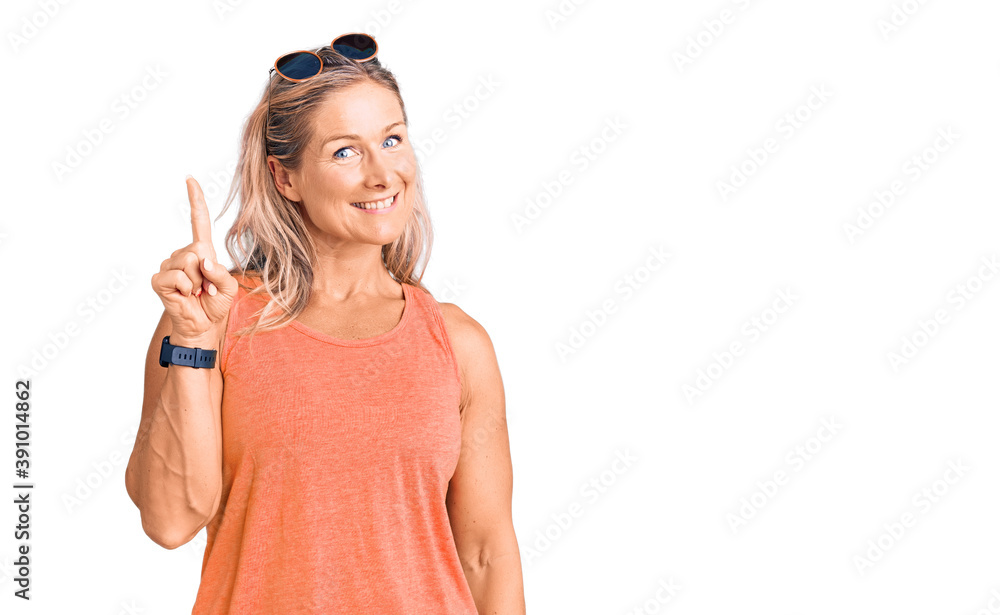 Middle age fit blonde woman wearing casual summer clothes and sunglasses pointing finger up with successful idea. exited and happy. number one. Middle age fit blonde woman wearing casual summer clothes and sunglasses pointing finger up with successful idea. exited and happy. number one.
