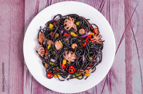 black spaghetti with seafood and vegetables on a white plate decorated with red pepper wooden background top view © Лозовая Людмила