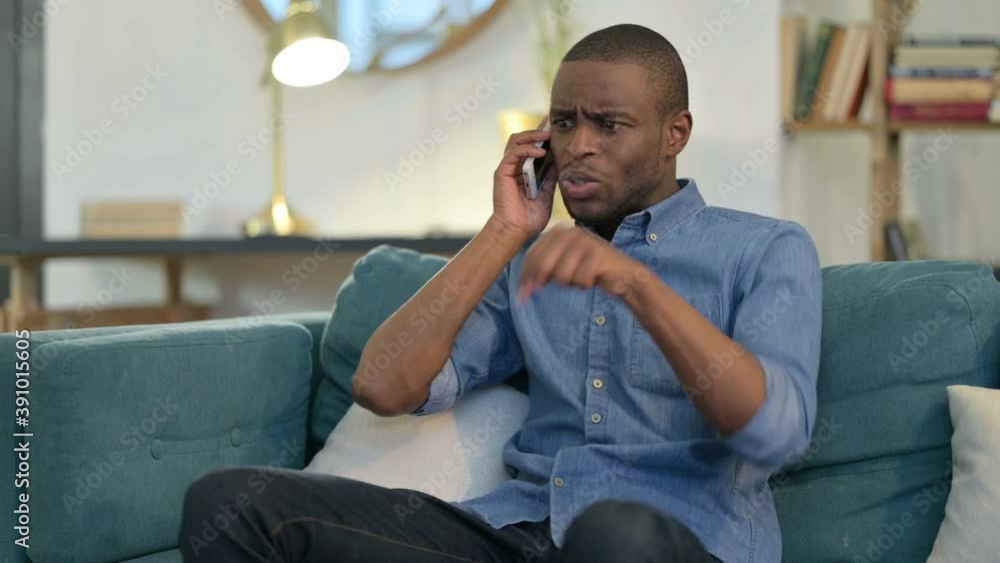 Young African Man Angry on Smartphone on Sofa Young African Man Angry on Smartphone on Sofa