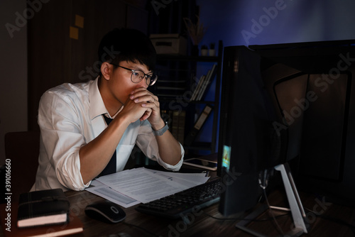 Attractive young asian businessman concentrated working until late overtime on publication at his desk in dark modern office at night, Overworking concept.