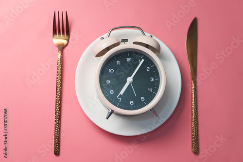 Alarm clock on plate on wooden table, top view.