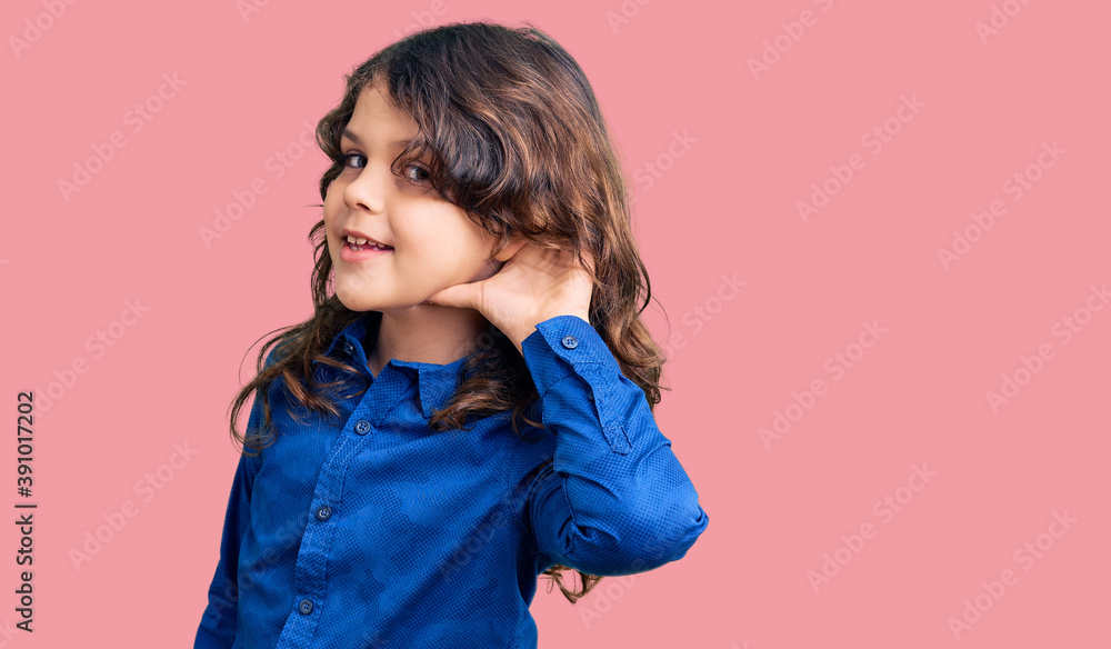 Cute child with long hair wearing casual clothes smiling with hand over ear listening an hearing to rumor or gossip. deafness concept. Cute child with long hair wearing casual clothes smiling with hand over ear listening an hearing to rumor or gossip. deafness concept.
