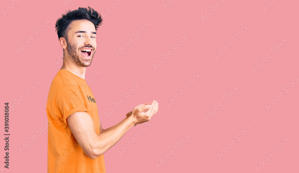 Young hispanic man wearing t shirt with happiness word message pointing aside with hands open palms showing copy space, presenting advertisement smiling excited happy Young hispanic man wearing t shirt with happiness word message pointing aside with hands open palms showing copy space, presenting advertisement smiling excited happy