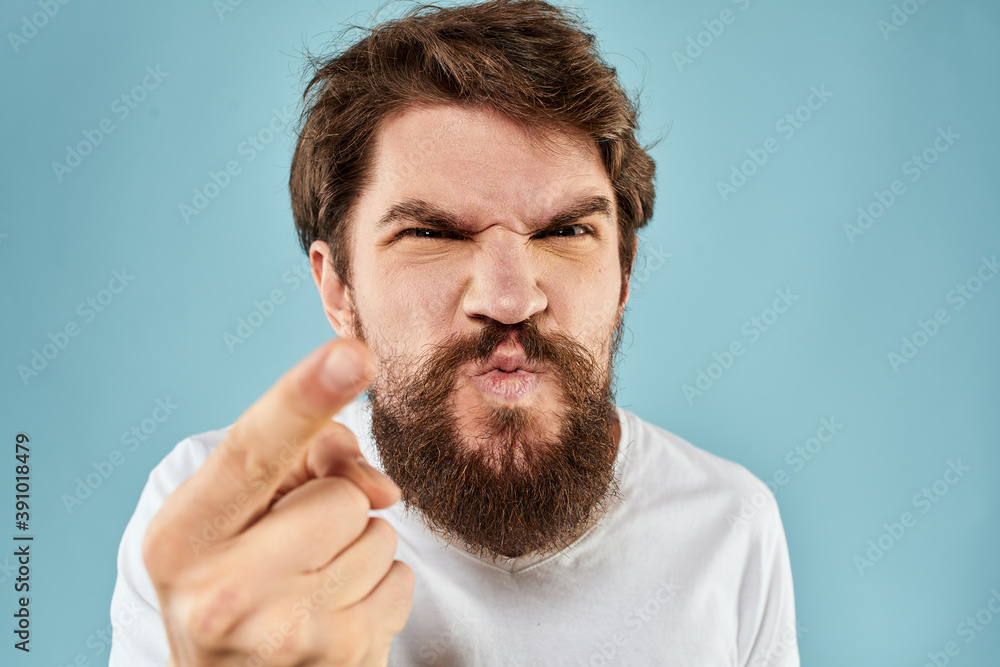 Bearded man in white T-shirt emotions gestures with hands displeased facial expression blue background Bearded man in white T-shirt emotions gestures with hands displeased facial expression blue background