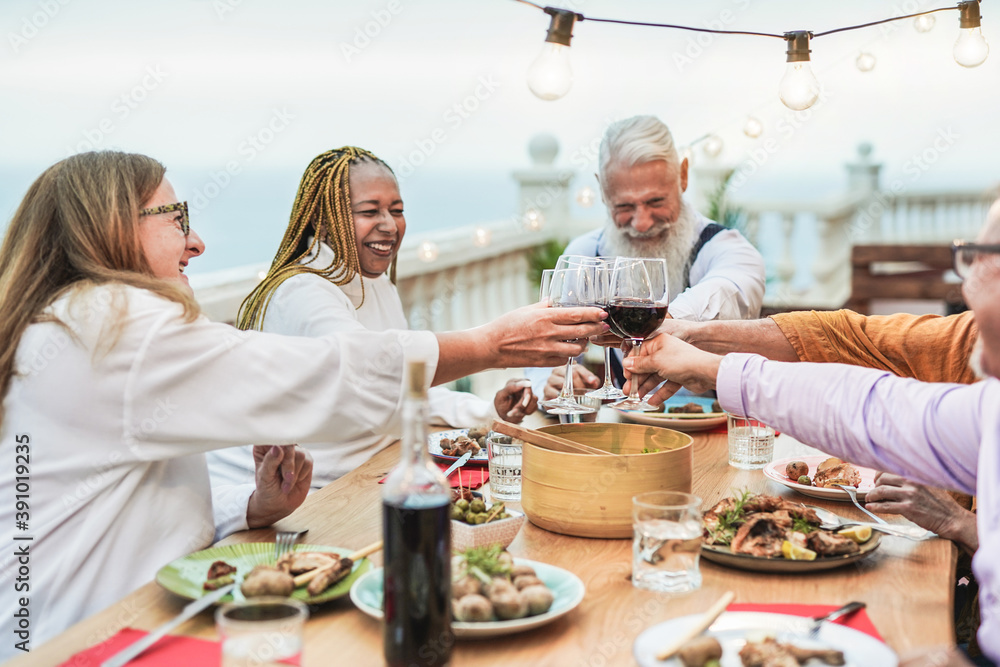 Multiracial senior people enjoy dinner at home on patio and cheering with wine