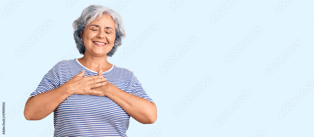 Senior woman with gray hair wearing casual striped clothes smiling with hands on chest with closed eyes and grateful gesture on face. health concept. Senior woman with gray hair wearing casual striped clothes smiling with hands on chest with closed eyes and grateful gesture on face. health concept.