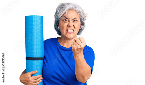 Obraz na plátne Senior woman with gray hair holding yoga mat annoyed and frustrated shouting wit