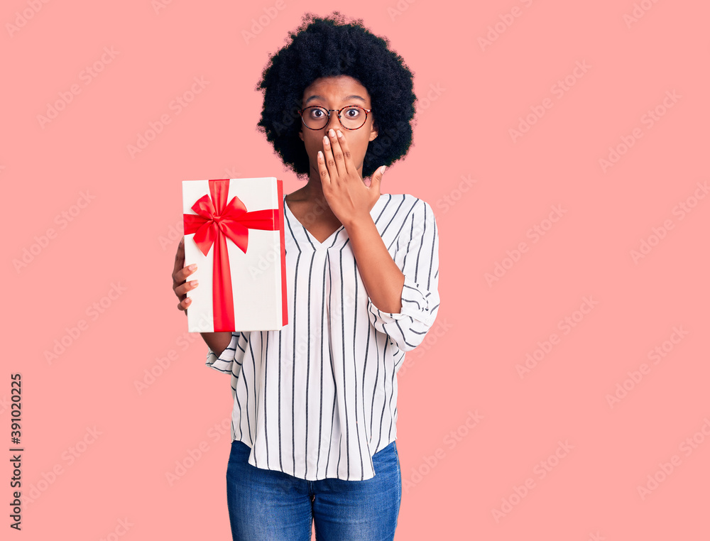 Young african american woman holding gift covering mouth with hand, shocked and afraid for mistake. surprised expression Young african american woman holding gift covering mouth with hand, shocked and afraid for mistake. surprised expression