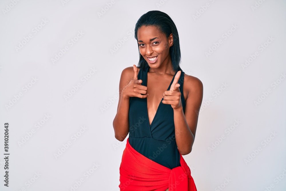 Young african american woman wearing swimsuit pointing fingers to camera with happy and funny face. good energy and vibes.