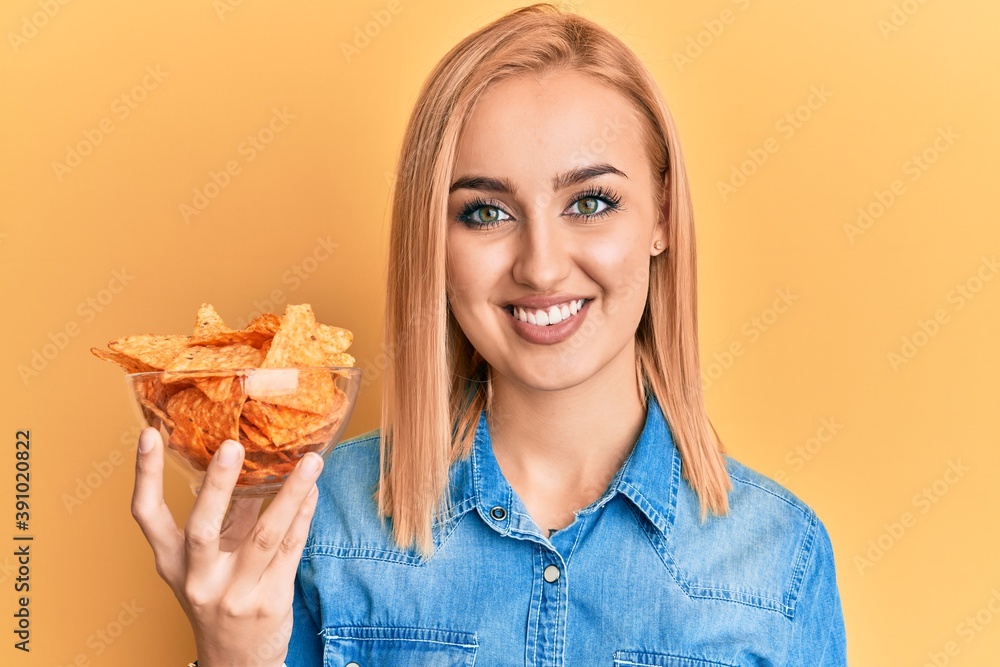 Beautiful caucasian woman holding nachos potato chips looking positive and happy standing and smiling with a confident smile showing teeth