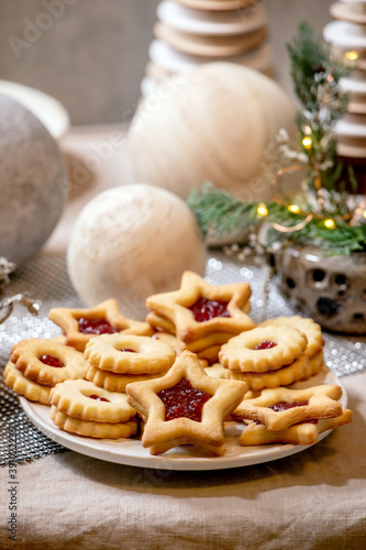 Homemade traditional Christmas Linz shortbread biscuits cookies with red jam on plate. Trend Wooden eco-friendly xmas decorations on linen tablecloth. Holiday table setting.