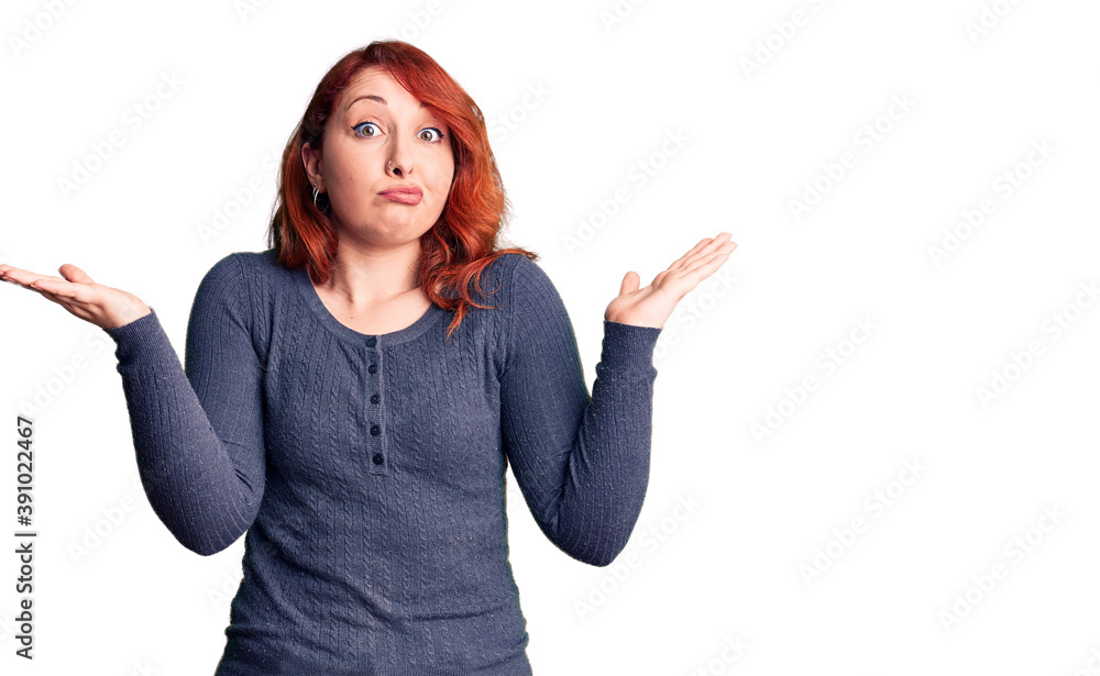 Young beautiful redhead woman wearing casual t-shirt clueless and confused expression with arms and hands raised. doubt concept. Young beautiful redhead woman wearing casual t-shirt clueless and confused expression with arms and hands raised. doubt concept.