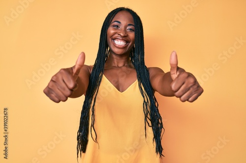 African american woman with braids wearing casual clothes approving doing positive gesture with hand, thumbs up smiling and happy for success. winner gesture.