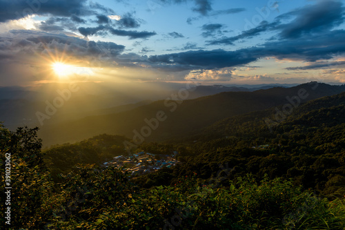 The bright rays of the sun are shining from saturated clouds to mountain range before sunset. © yotrakbutda