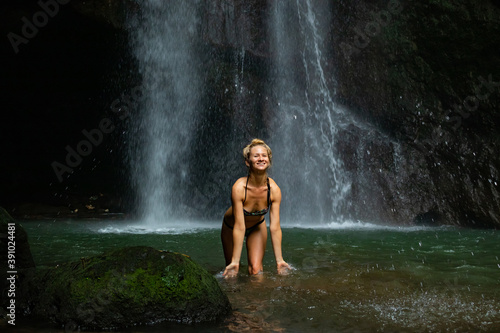 Young Caucasian woman with blond hair standing near the waterfall. Travel lifestyle. Leke Leke waterfall, Bali.
