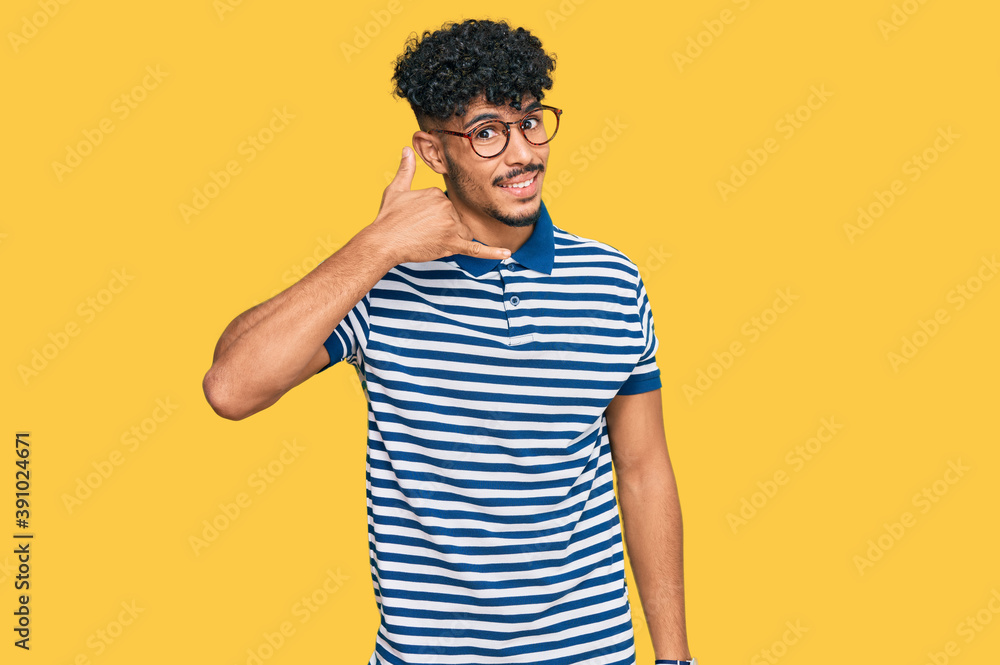 Young arab man wearing casual clothes and glasses smiling doing phone gesture with hand and fingers like talking on the telephone. communicating concepts. Young arab man wearing casual clothes and glasses smiling doing phone gesture with hand and fingers like talking on the telephone. communicating concepts.
