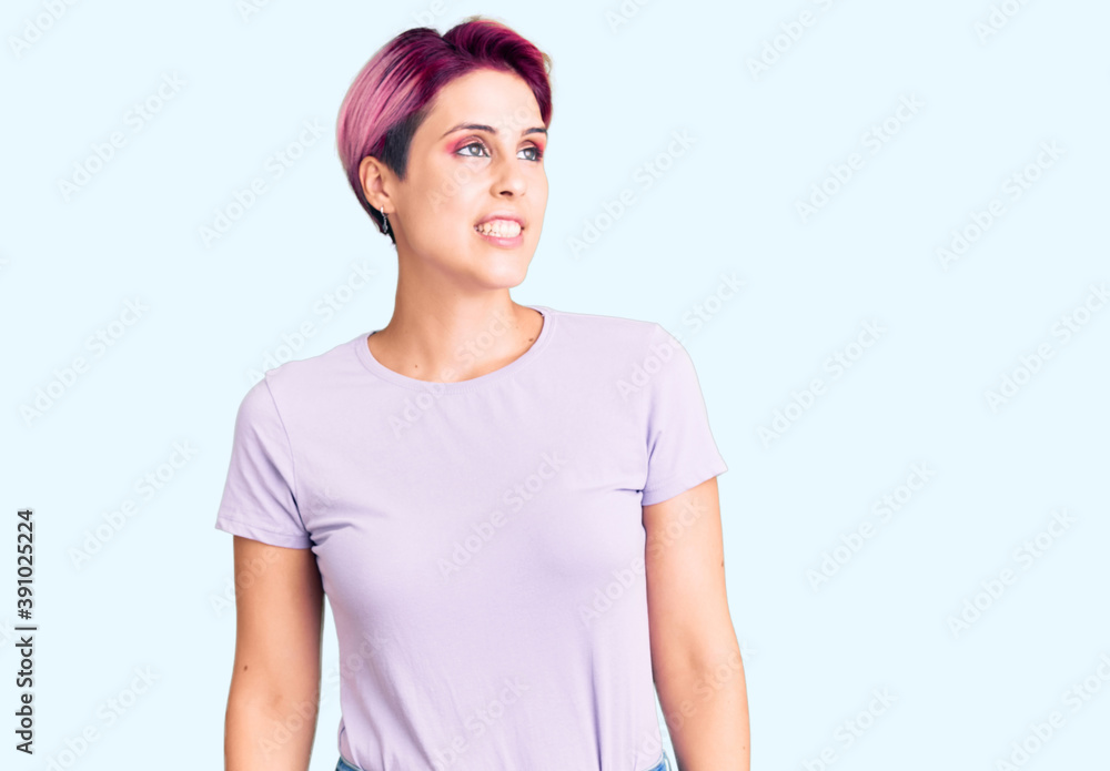 Young beautiful woman with pink hair wearing casual clothes looking away to side with smile on face, natural expression. laughing confident. Young beautiful woman with pink hair wearing casual clothes looking away to side with smile on face, natural expression. laughing confident.