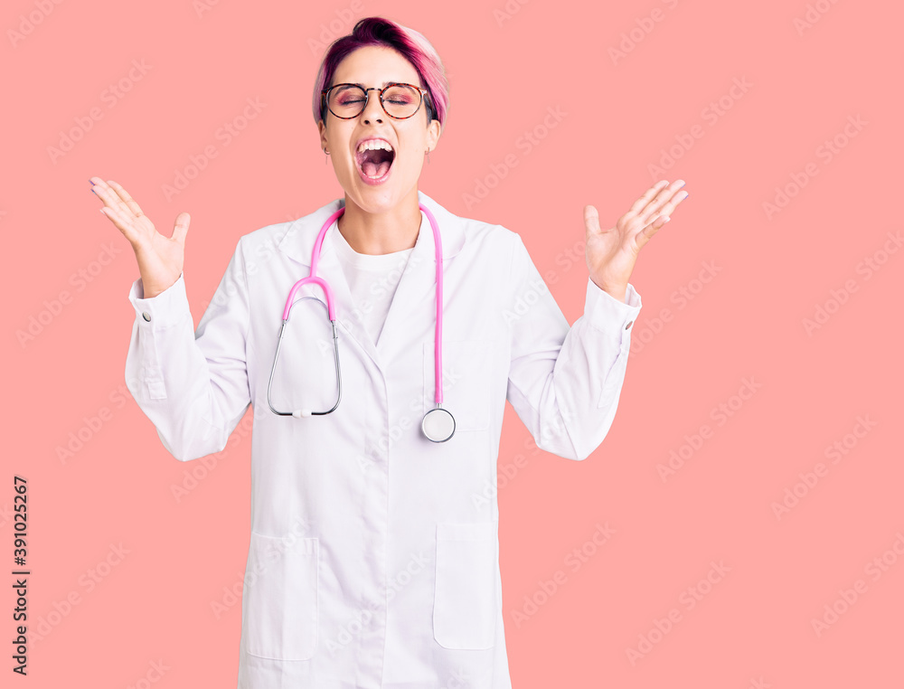 Young beautiful woman with pink hair wearing doctor uniform celebrating mad and crazy for success with arms raised and closed eyes screaming excited. winner concept Young beautiful woman with pink hair wearing doctor uniform celebrating mad and crazy for success with arms raised and closed eyes screaming excited. winner concept