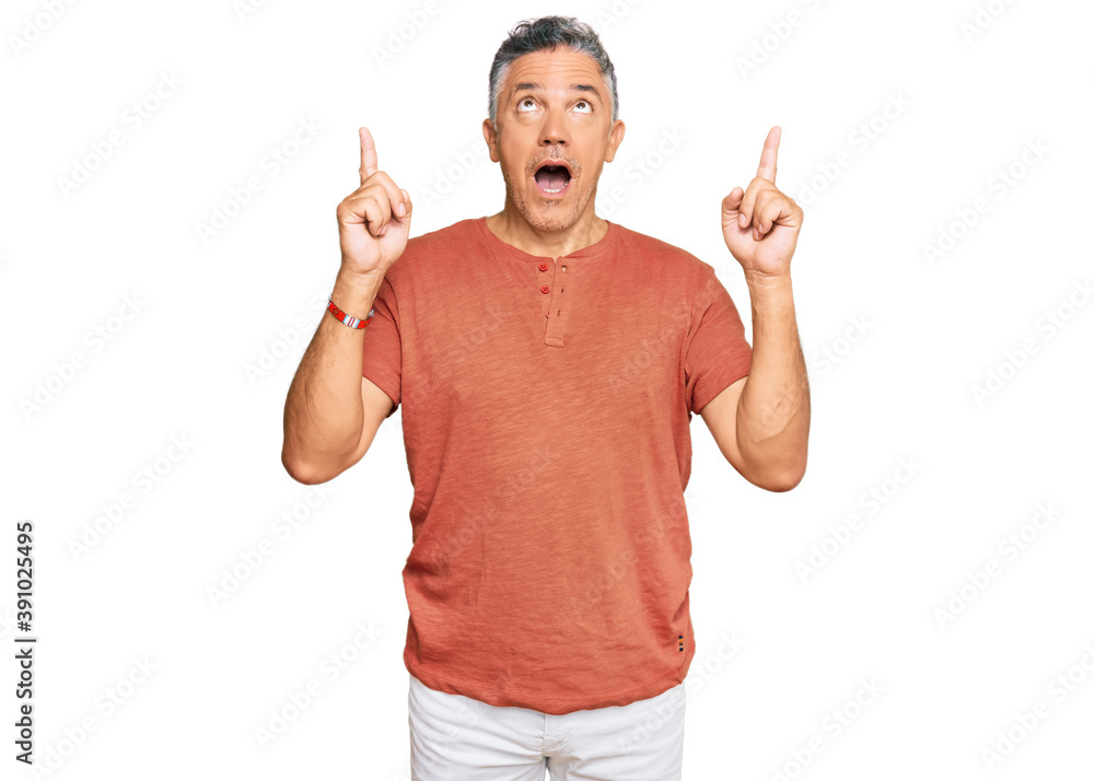 Naklejka premium Handsome middle age man wearing casual clothes amazed and surprised looking up and pointing with fingers and raised arms.