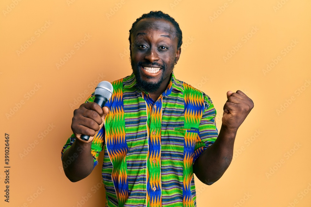 Handsome young black man singing song using microphone screaming proud, celebrating victory and success very excited with raised arm Handsome young black man singing song using microphone screaming proud, celebrating victory and success very excited with raised arm