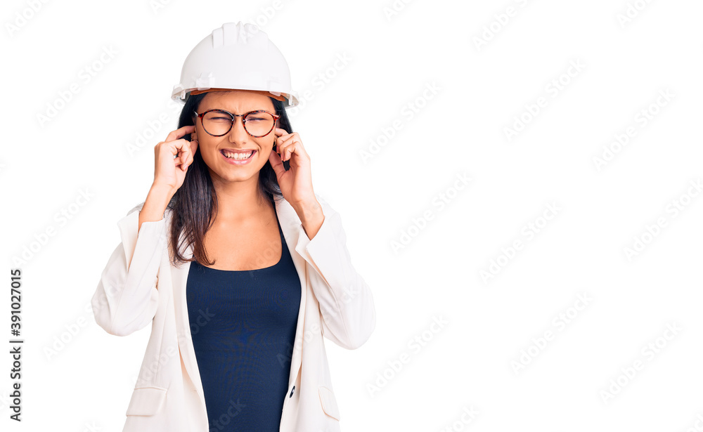 Young beautiful latin girl wearing architect hardhat and glasses covering ears with fingers with annoyed expression for the noise of loud music. deaf concept. Young beautiful latin girl wearing architect hardhat and glasses covering ears with fingers with annoyed expression for the noise of loud music. deaf concept.