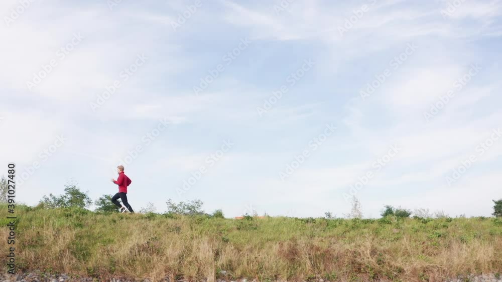 Young man running by the road with blue sky background. Sporty people activities and a healthy lifestyle concept 4K footage.