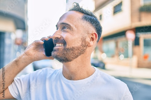 Middle age handsome man smiling happy using smartphone at the city.