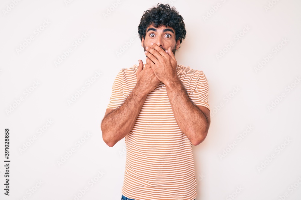 Handsome young man with curly hair and bear wearing casual striped tshirt shocked covering mouth with hands for mistake. secret concept. Handsome young man with curly hair and bear wearing casual striped tshirt shocked covering mouth with hands for mistake. secret concept.