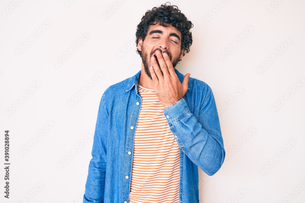 Handsome young man with curly hair and bear wearing casual denim jacket bored yawning tired covering mouth with hand. restless and sleepiness. Handsome young man with curly hair and bear wearing casual denim jacket bored yawning tired covering mouth with hand. restless and sleepiness.