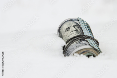 A dollar in winter, a roll of twisted dollar bills lying on the snow, close-up.