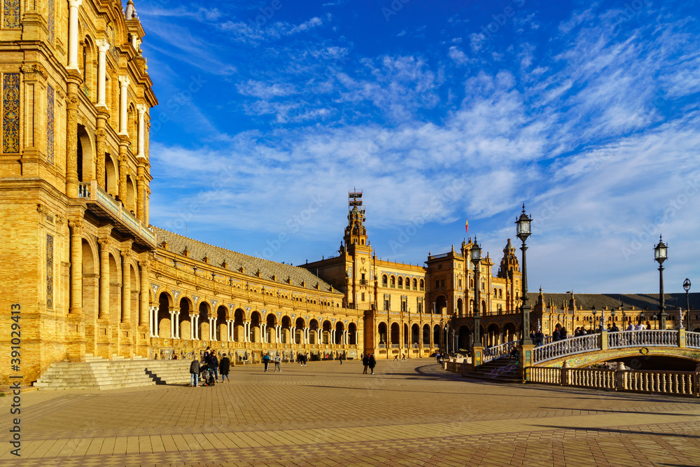 Fototapeta premium Plaza de España en Sevilla al atardecer en un día soleado con nubes y gente paseando y disfrutando del buen tiempo.