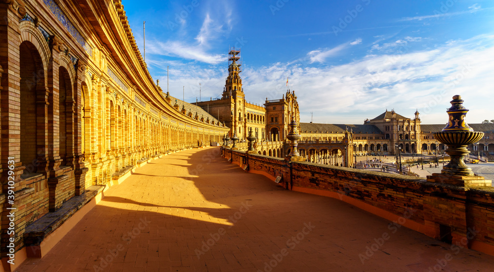 Obraz premium Plaza de España en Sevilla al atardecer en un día soleado con nubes y gente paseando y disfrutando del buen tiempo.