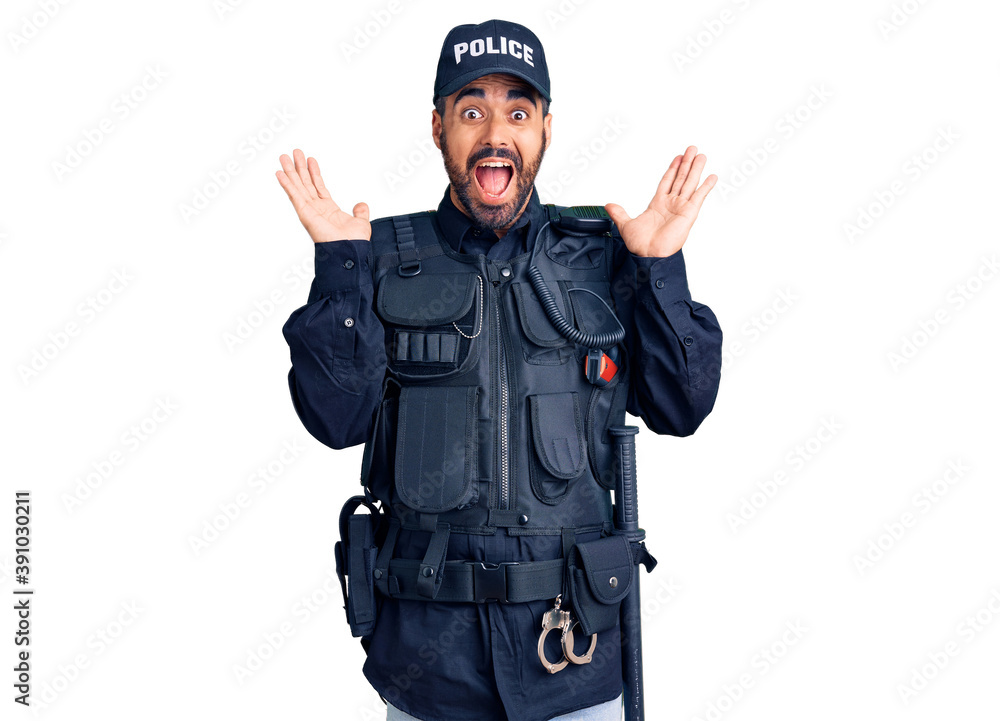 Young hispanic man wearing police uniform celebrating crazy and amazed for success with arms raised and open eyes screaming excited. winner concept Young hispanic man wearing police uniform celebrating crazy and amazed for success with arms raised and open eyes screaming excited. winner concept