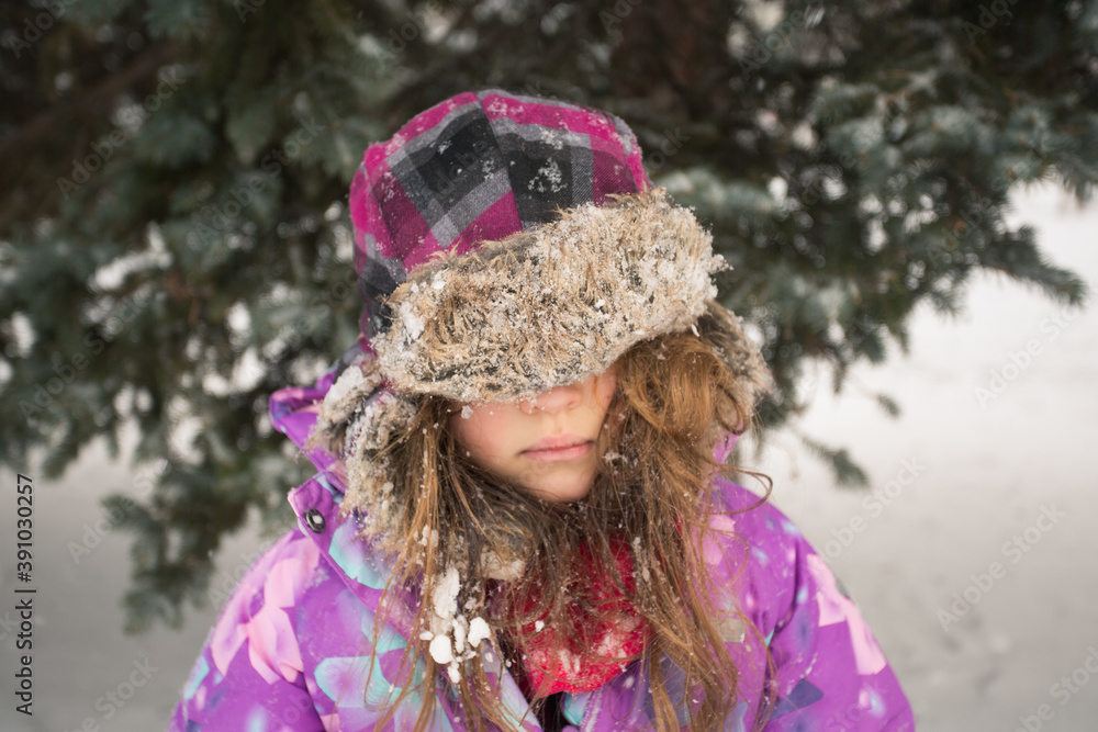 Little girl with winter hat on her eyes near fir tree. At snowy day Little girl with winter hat on her eyes near fir tree. At snowy day