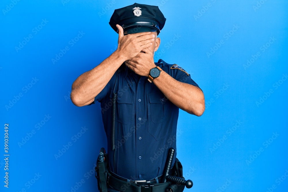 Middle age handsome man wearing police uniform covering eyes and mouth with hands, surprised and shocked. hiding emotion Middle age handsome man wearing police uniform covering eyes and mouth with hands, surprised and shocked. hiding emotion