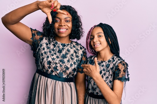 Beautiful african american mother and daughter wearing sexy party dress smiling making frame with hands and fingers with happy face. creativity and photography concept. photo