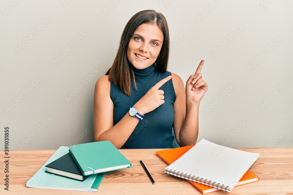 Young caucasian woman studying for exam smiling and looking at the camera pointing with two hands and fingers to the side. Young caucasian woman studying for exam smiling and looking at the camera pointing with two hands and fingers to the side.