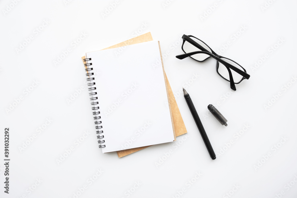 Blank notebook is on top of white office desk table with pen and eye glasses. Top view, flat lay. Blank notebook is on top of white office desk table with pen and eye glasses. Top view, flat lay.