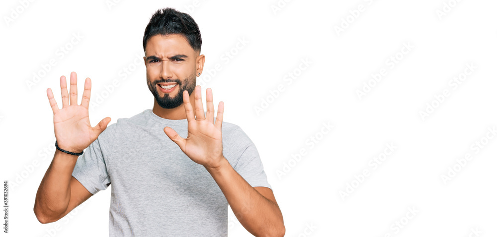 Young man with beard wearing casual grey tshirt afraid and terrified with fear expression stop gesture with hands, shouting in shock. panic concept. Young man with beard wearing casual grey tshirt afraid and terrified with fear expression stop gesture with hands, shouting in shock. panic concept.