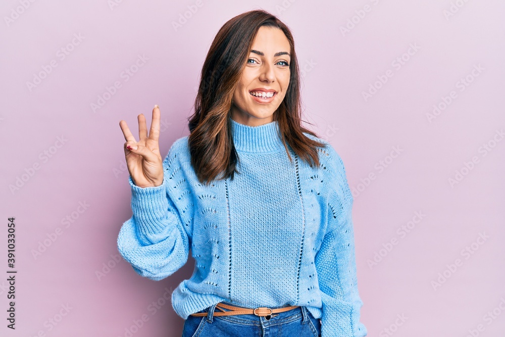 Young brunette woman wearing casual winter sweater over pink background showing and pointing up with fingers number three while smiling confident and happy. Young brunette woman wearing casual winter sweater over pink background showing and pointing up with fingers number three while smiling confident and happy.